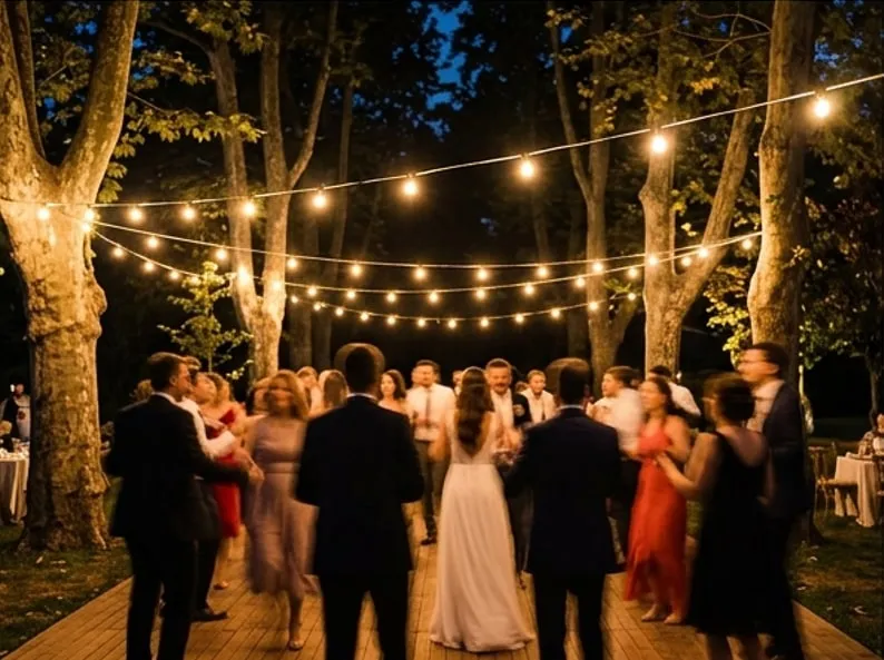 Gece ağaçlar arasına gerilmiş ampullerin altında dans eden davetliler